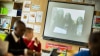 Kids in a classroom looking at an image of kids on a big screen