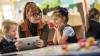 A school teacher in a classroom with a couple of young students looking at a computer tablet